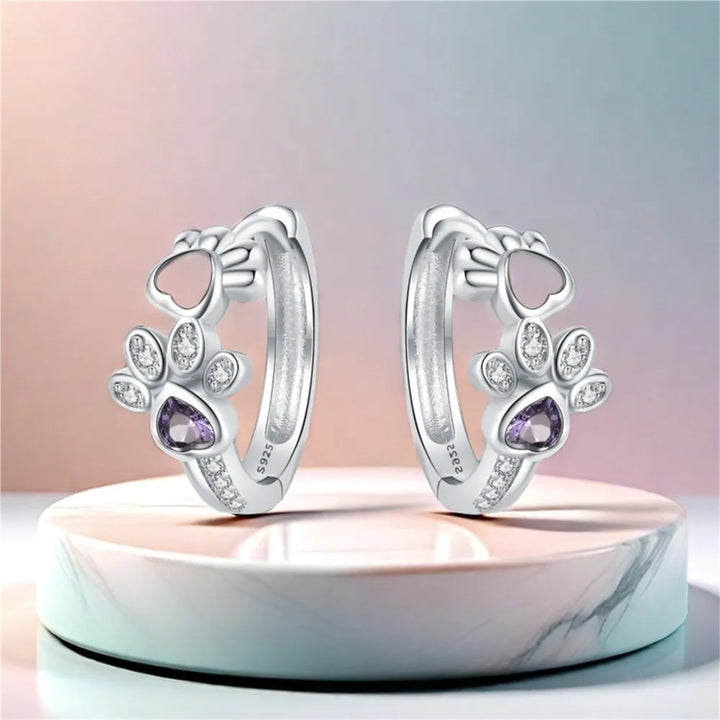 Ohrringe mit Pfotenabdruck in Silber, mit Zirkonia und einem herzförmigen Edelstein.